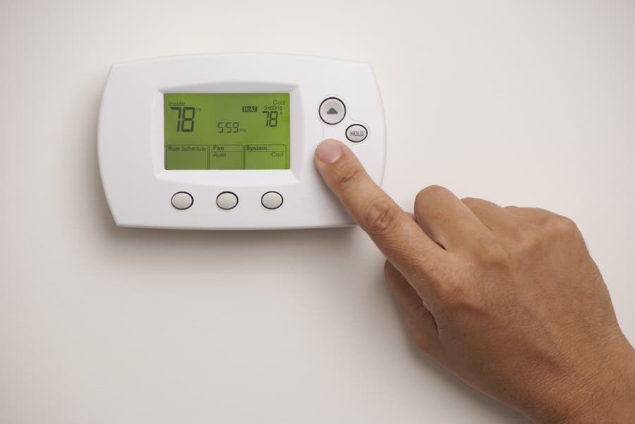 A hand pressing a button on a wall thermostat with a green backlit display reading 78 degrees.